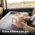 Toddler holding the Activity Cube on a car seat tray while travelling